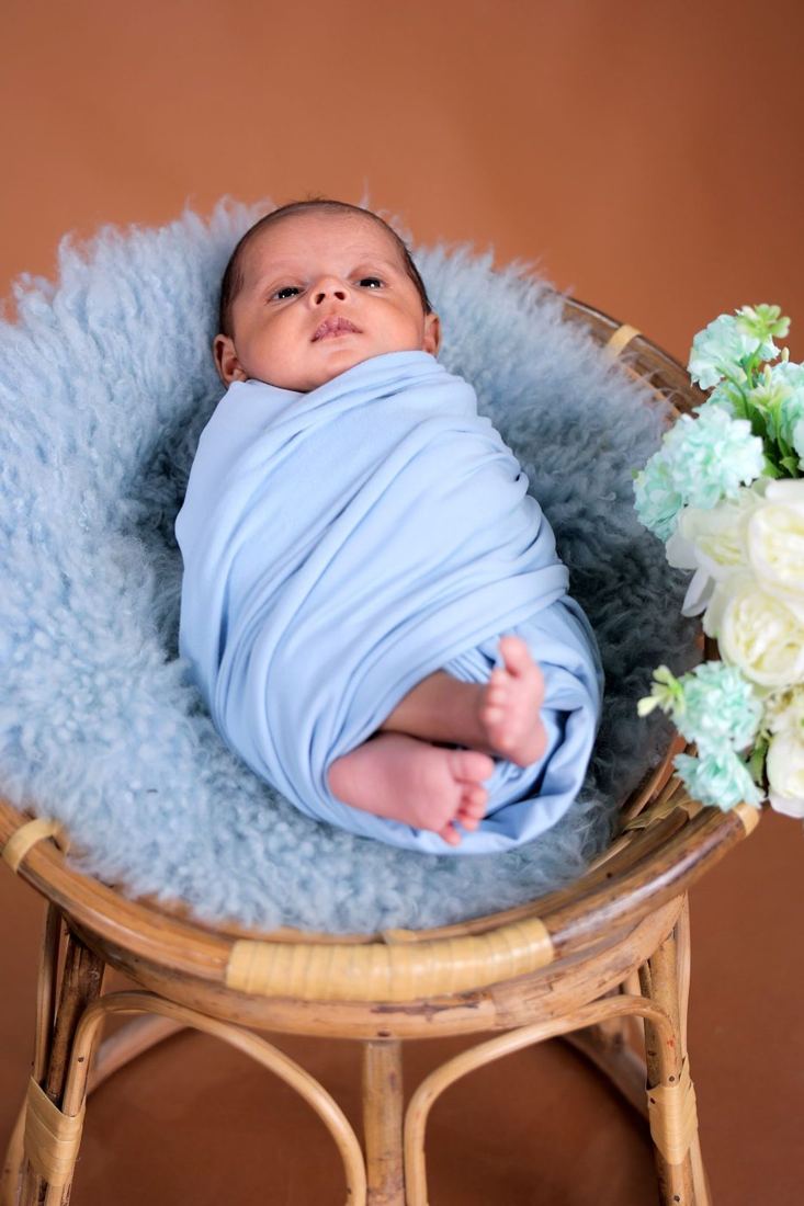 Baby in a blue wrap on a small chair with flowers