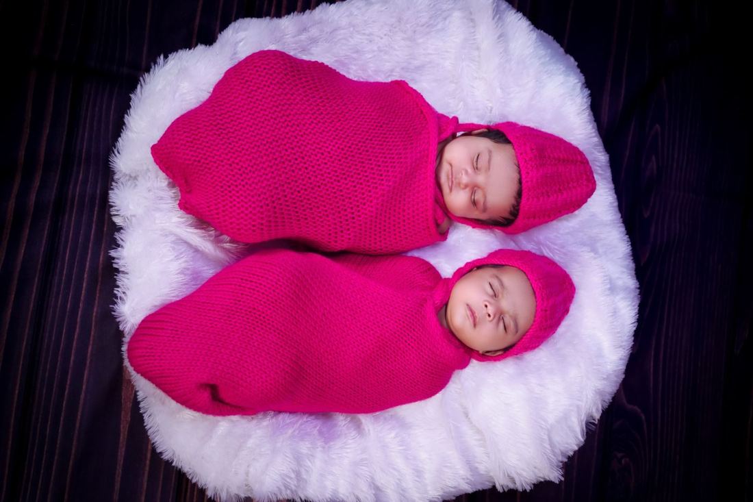Twin newborns asleep in pink knit swaddles